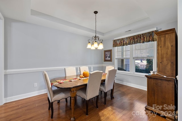 dining room with a notable chandelier, dark hardwood / wood-style floors, and a raised ceiling