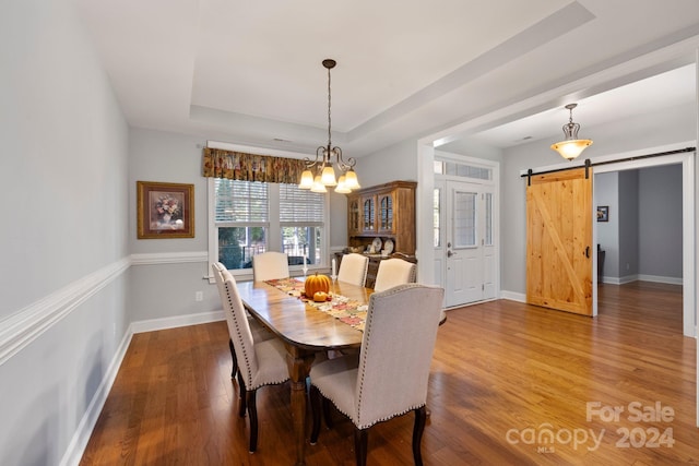 dining room with an inviting chandelier, a barn door, hardwood / wood-style flooring, and a tray ceiling