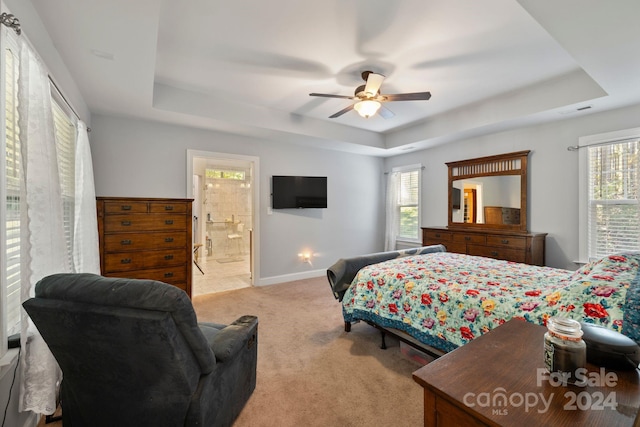 bedroom with light carpet, multiple windows, a tray ceiling, and ceiling fan