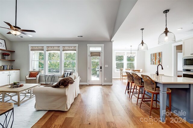 living room with ceiling fan, sink, light hardwood / wood-style floors, and vaulted ceiling