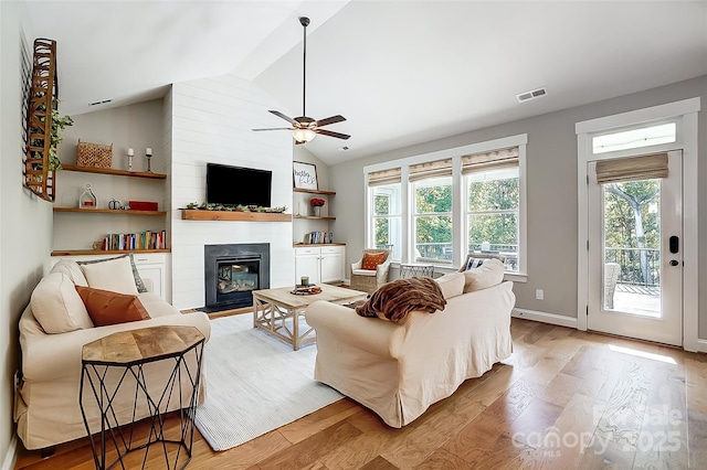 living room with visible vents, a large fireplace, light wood-type flooring, and vaulted ceiling