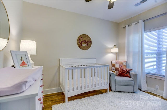 bedroom with dark wood-type flooring, ceiling fan, and a nursery area