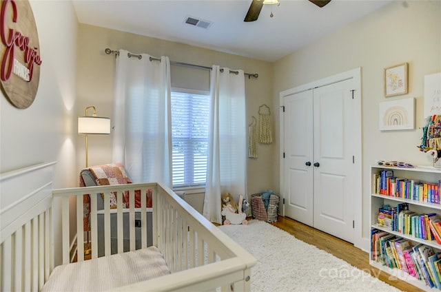 bedroom with a closet, ceiling fan, a crib, and hardwood / wood-style floors