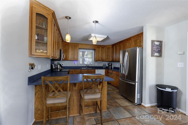 kitchen featuring appliances with stainless steel finishes, a textured ceiling, a kitchen bar, sink, and decorative light fixtures