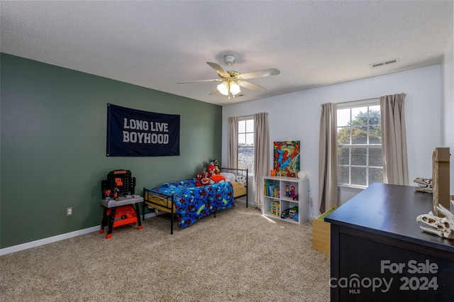 carpeted bedroom with a textured ceiling, multiple windows, and ceiling fan