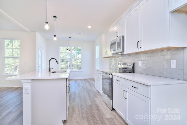 kitchen with an island with sink, stainless steel appliances, sink, pendant lighting, and light wood-type flooring