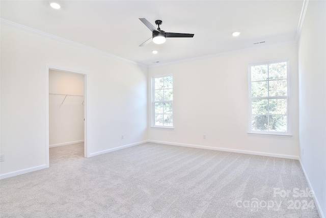 unfurnished bedroom with light carpet, a walk in closet, crown molding, and ceiling fan