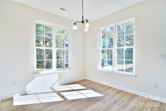 empty room with a healthy amount of sunlight, light hardwood / wood-style flooring, and an inviting chandelier