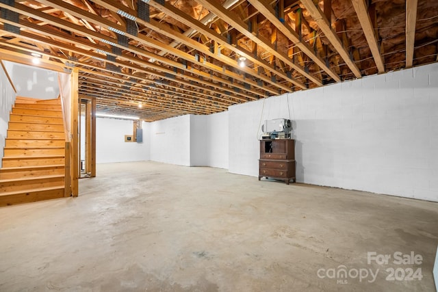unfinished below grade area featuring concrete block wall, stairway, and electric panel