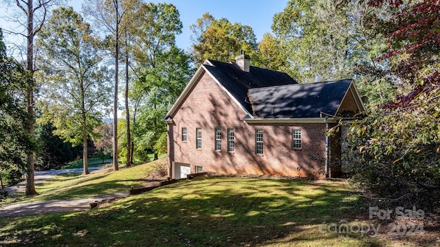 view of side of property featuring roof with shingles, an attached garage, brick siding, a chimney, and a lawn