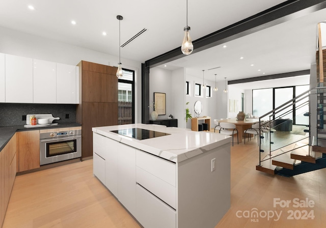 kitchen with a kitchen island, oven, hanging light fixtures, light wood-type flooring, and white cabinets