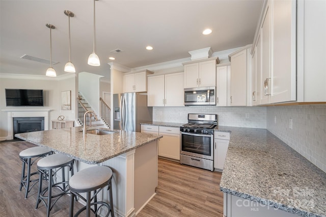 kitchen with a center island with sink, light hardwood / wood-style flooring, sink, pendant lighting, and appliances with stainless steel finishes