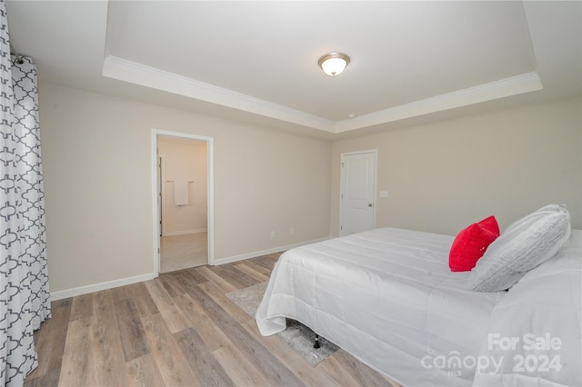 bedroom featuring light wood-type flooring, a tray ceiling, and connected bathroom