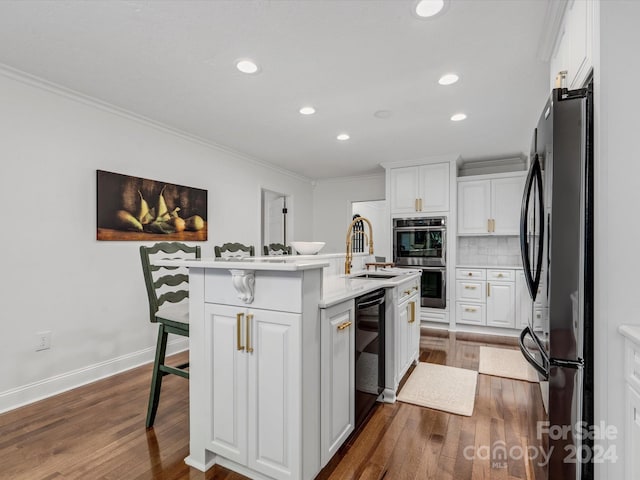 kitchen featuring a breakfast bar, white cabinets, a center island with sink, and refrigerator