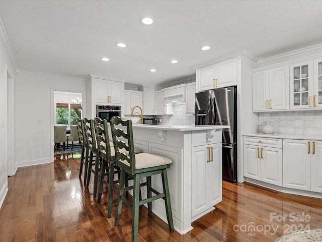 kitchen with white cabinets, tasteful backsplash, a center island with sink, dark hardwood / wood-style flooring, and appliances with stainless steel finishes