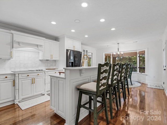 kitchen with pendant lighting, white cabinets, hardwood / wood-style flooring, stainless steel fridge with ice dispenser, and a center island with sink