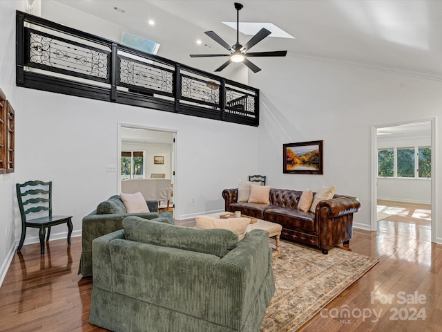 living room with hardwood / wood-style flooring, high vaulted ceiling, a skylight, and ceiling fan