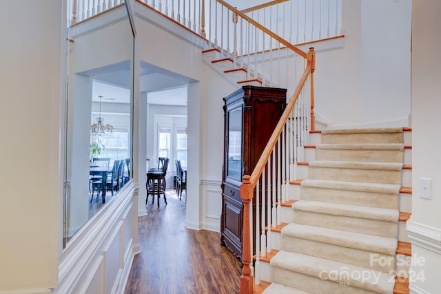 stairs with a towering ceiling, an inviting chandelier, and hardwood / wood-style flooring