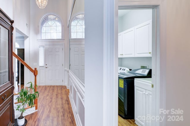 foyer entrance with light hardwood / wood-style flooring, washing machine and dryer, and an inviting chandelier