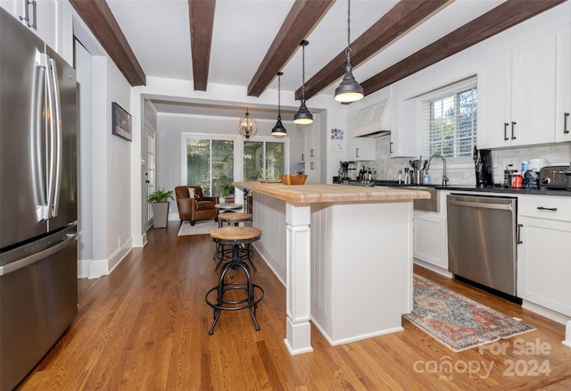 kitchen with stainless steel appliances, a kitchen island, wood counters, hanging light fixtures, and white cabinets