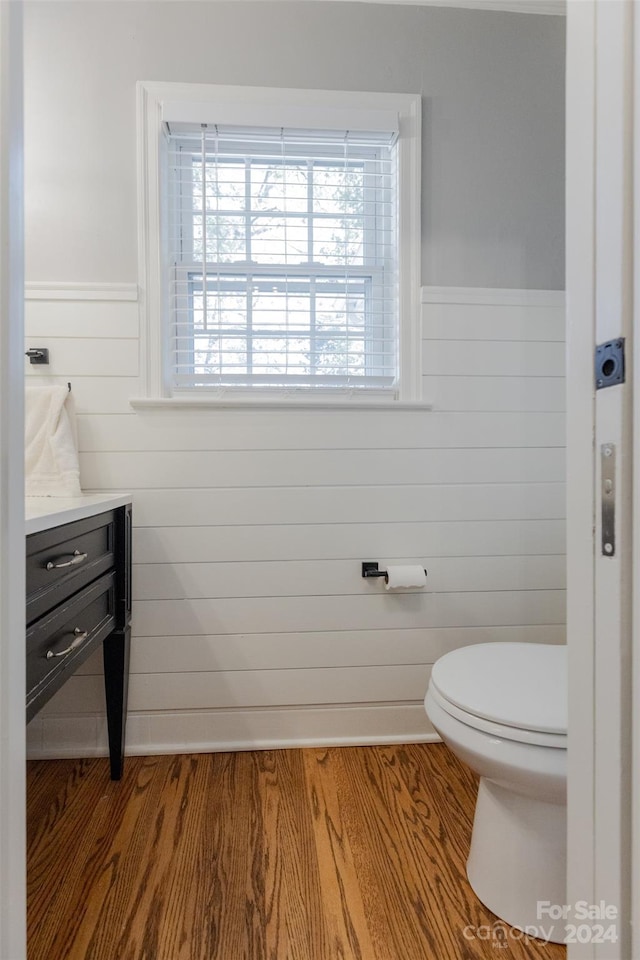 bathroom with toilet, wood walls, vanity, and hardwood / wood-style flooring