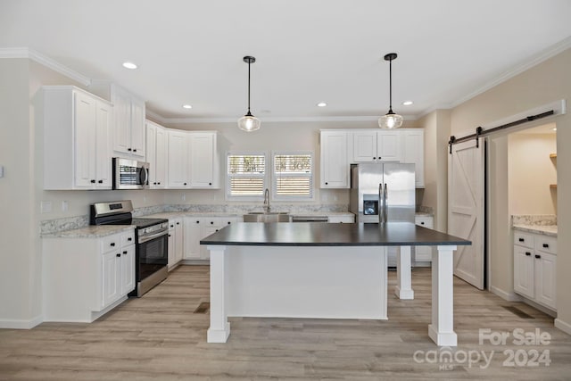 kitchen with stainless steel appliances, sink, a barn door, white cabinetry, and hanging light fixtures