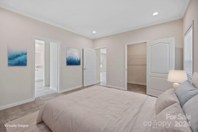 bedroom with light carpet, ensuite bathroom, crown molding, a spacious closet, and a closet