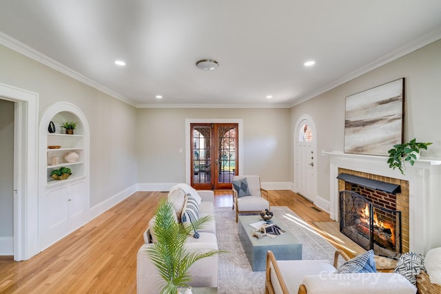 living room with built in shelves, french doors, ornamental molding, light wood-type flooring, and a brick fireplace