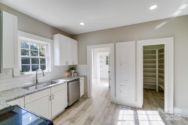 kitchen featuring backsplash, dishwasher, sink, white cabinetry, and light stone counters