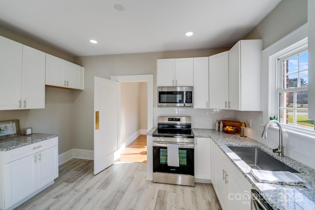 kitchen featuring stainless steel appliances, white cabinets, light stone counters, and sink