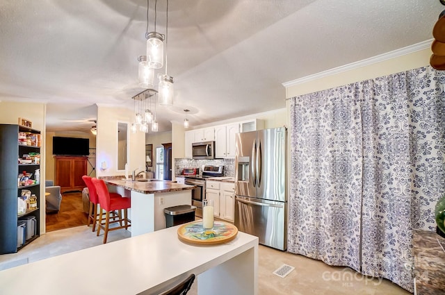 kitchen with pendant lighting, appliances with stainless steel finishes, a kitchen island with sink, and white cabinetry