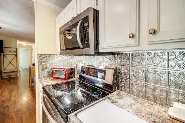 kitchen featuring appliances with stainless steel finishes, a textured ceiling, white cabinetry, wood-type flooring, and ornamental molding