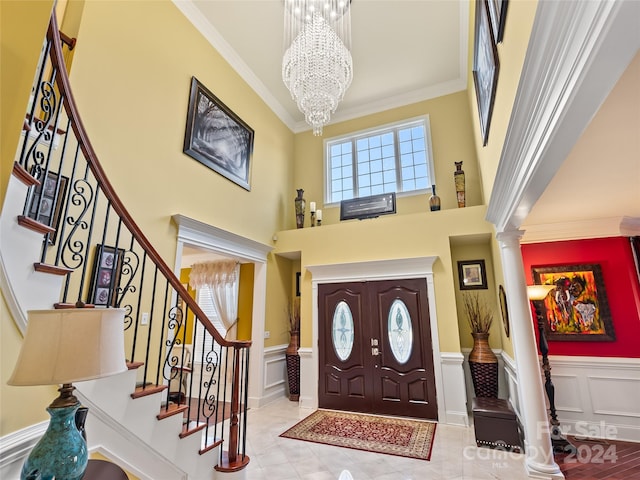 foyer entrance with a chandelier, a high ceiling, ornate columns, and crown molding