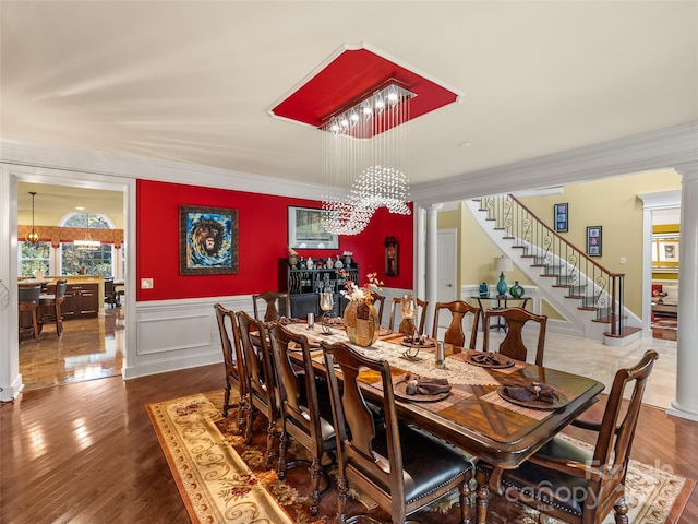 dining space with dark hardwood / wood-style flooring, crown molding, a notable chandelier, and ornate columns