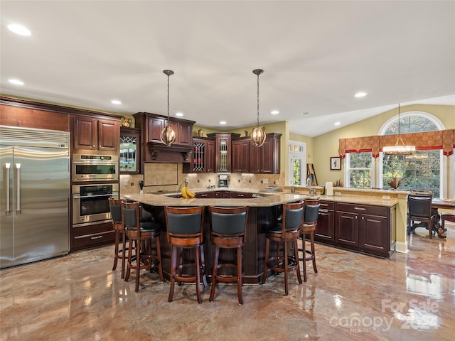 kitchen featuring hanging light fixtures, stainless steel appliances, tasteful backsplash, an island with sink, and vaulted ceiling