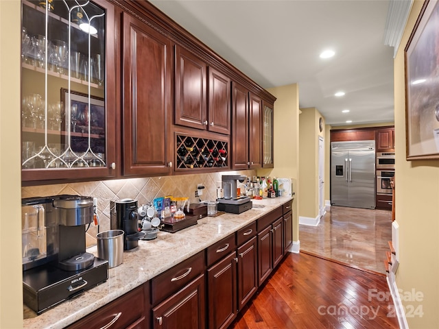 bar with tasteful backsplash, light stone countertops, stainless steel appliances, and dark hardwood / wood-style floors