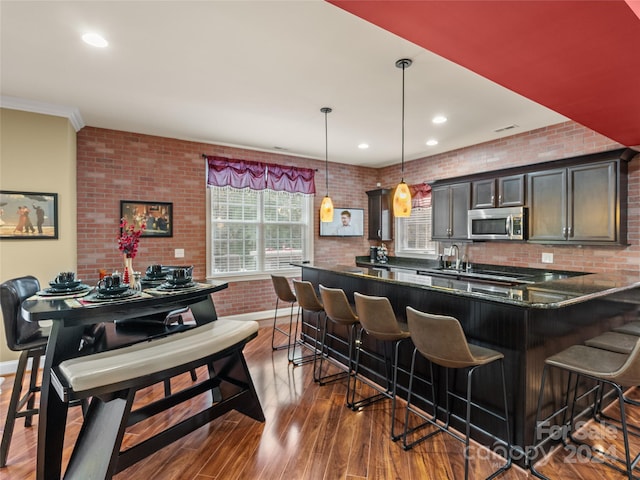 kitchen with a kitchen breakfast bar, dark hardwood / wood-style flooring, brick wall, dark brown cabinetry, and hanging light fixtures