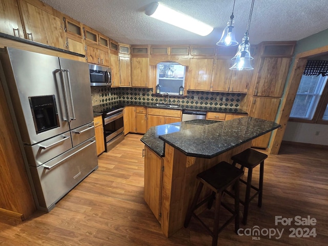 kitchen with a center island, hanging light fixtures, sink, light wood-type flooring, and appliances with stainless steel finishes