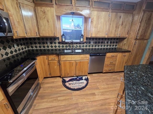 kitchen featuring stainless steel appliances, light hardwood / wood-style floors, sink, tasteful backsplash, and dark stone counters