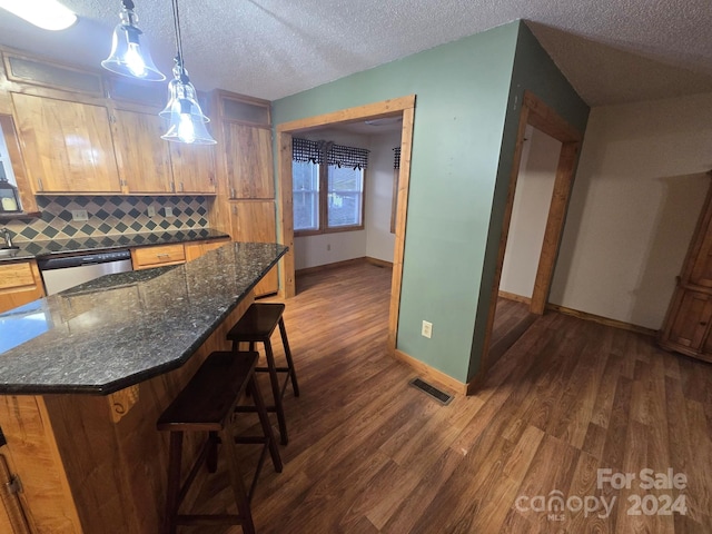 kitchen with tasteful backsplash, a kitchen bar, dark hardwood / wood-style floors, a textured ceiling, and dishwasher