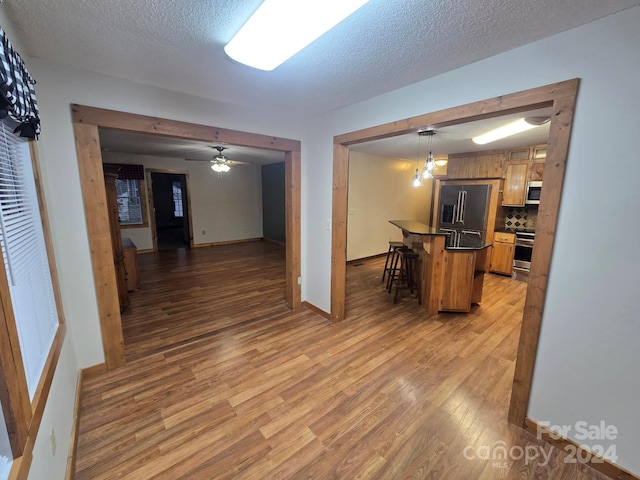 kitchen with hanging light fixtures, a kitchen breakfast bar, ceiling fan, light wood-type flooring, and appliances with stainless steel finishes