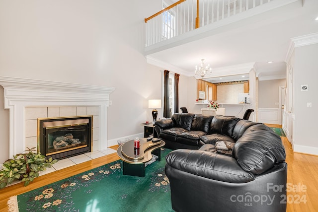 living room with a tiled fireplace, hardwood / wood-style flooring, crown molding, an inviting chandelier, and a towering ceiling