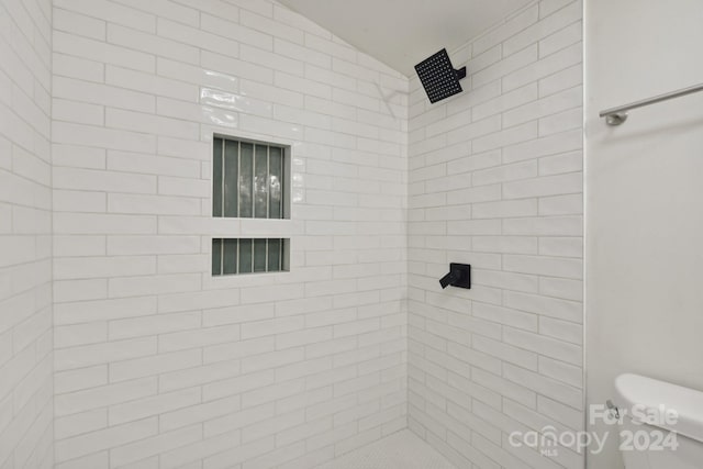 bathroom with toilet, a tile shower, and vaulted ceiling