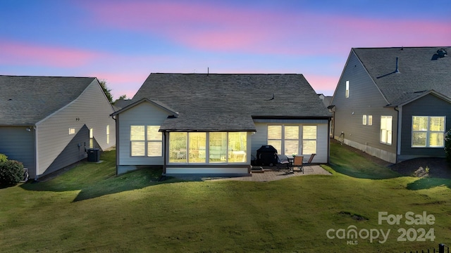 back house at dusk featuring a patio area, a sunroom, and a lawn