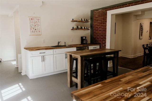 bar with wood counters, white cabinetry, sink, and dishwasher