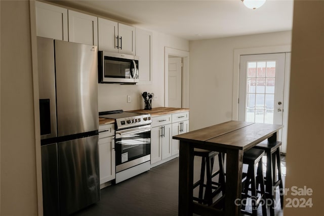 kitchen featuring butcher block counters, dark hardwood / wood-style flooring, appliances with stainless steel finishes, and white cabinets