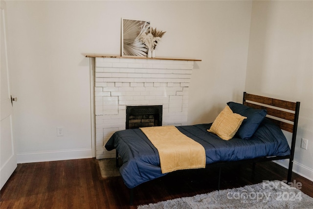 bedroom with a brick fireplace and dark hardwood / wood-style floors