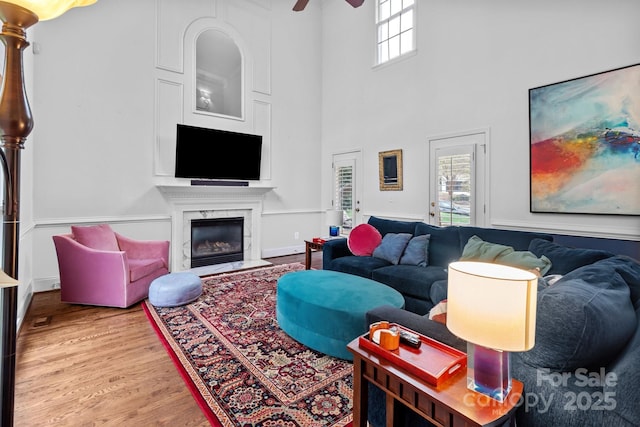 living room with ceiling fan, wood-type flooring, a premium fireplace, and a high ceiling