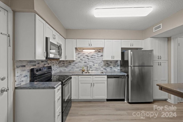 kitchen featuring stainless steel appliances, sink, light wood-type flooring, white cabinetry, and a textured ceiling