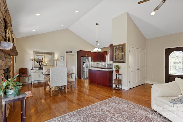 living room featuring ceiling fan, a stone fireplace, high vaulted ceiling, and dark hardwood / wood-style flooring